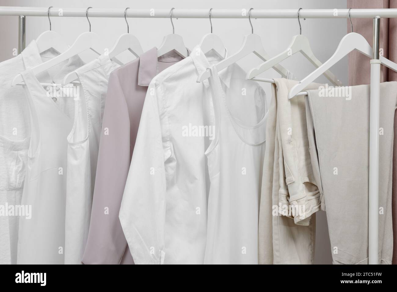 Rack with different stylish women`s clothes near white wall Stock Photo